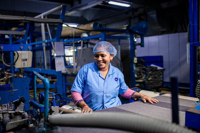A happy female factory worker in a hairnet and uniform, working at a machine, highlighting coworker interactions.