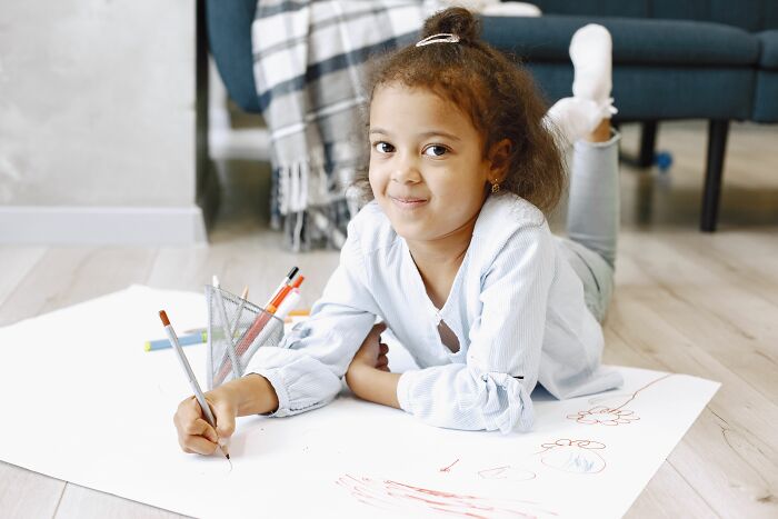 A young girl smiling, lying on the floor drawing, delivering sick burns with her creativity.