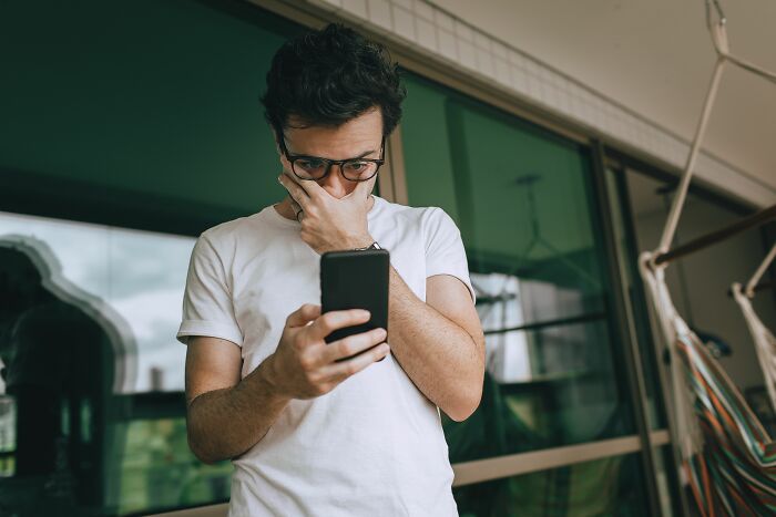 A man looking shocked while holding his phone, reacting to spicy personal details from his coworkers, possibly in PTSD mode.
