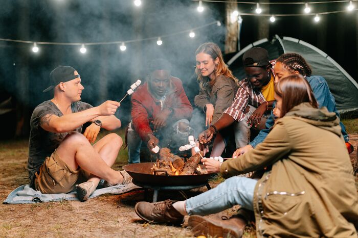 Friends gathered around a campfire, roasting marshmallows, highlighting the social and recreational aspects of life in America that newcomers enjoy.