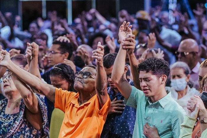 People with raised hands during a gathering, possibly showing a misconception about group belief.