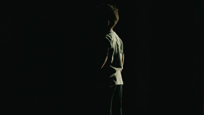 A small child standing in darkness with a faint light on his back, suggesting scary true stories.