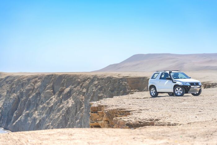 A white SUV parked precariously close to a cliff edge, symbolizing the line between life and what comes after.