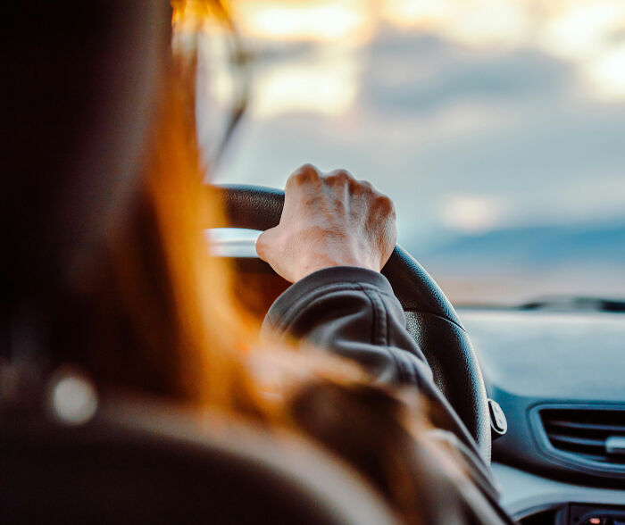 A person with auburn hair driving a car at sunset, representing the act of driving a car where a baby might be left. A person with auburn hair driving a car at sunset, representing the act of driving a car where a baby might be left.