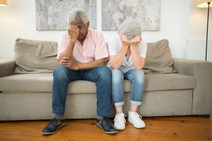 An elderly couple sits on a couch with their heads in their hands, looking distressed. Horrible parent.