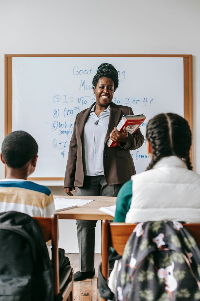 A smiling teacher in front of a whiteboard with students, illustrating the education system in America that can surprise newcomers.