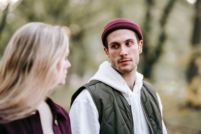 A serious-looking man in a beanie and vest looking at a woman, representing a pivotal relationship moment.