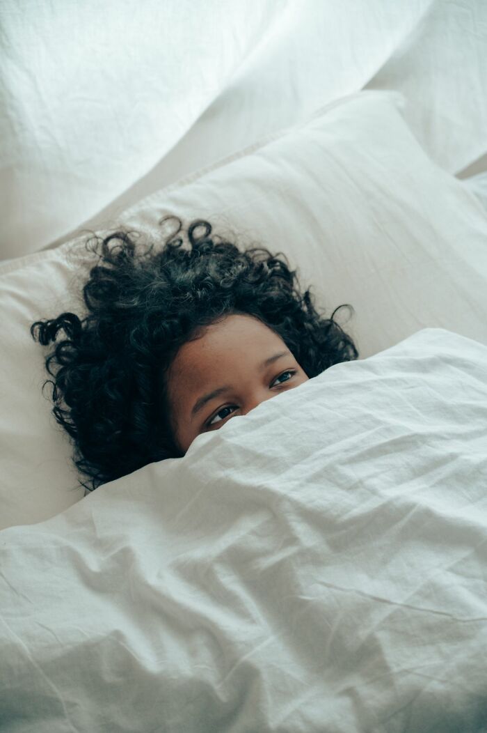 A child peeking out from under a white duvet, experiencing scary true stories.