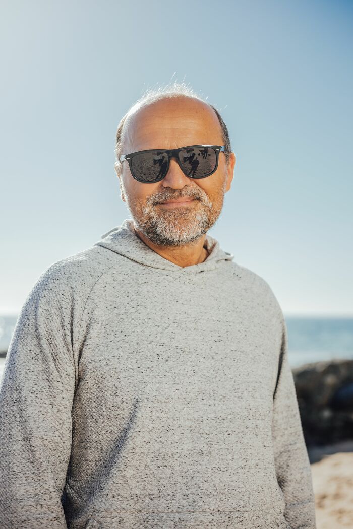 A man in sunglasses at the beach, smiling, embodying incredible accomplishments and motivation.