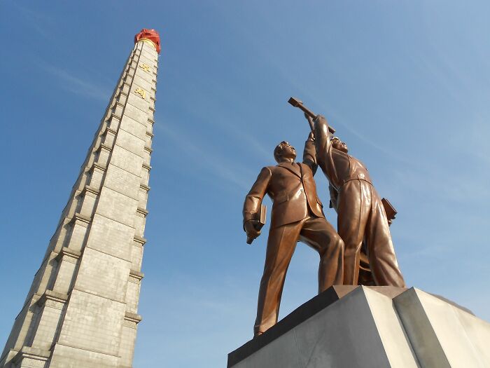A towering monument and bronze statues against a blue sky, representing beliefs and the impact of propaganda.
