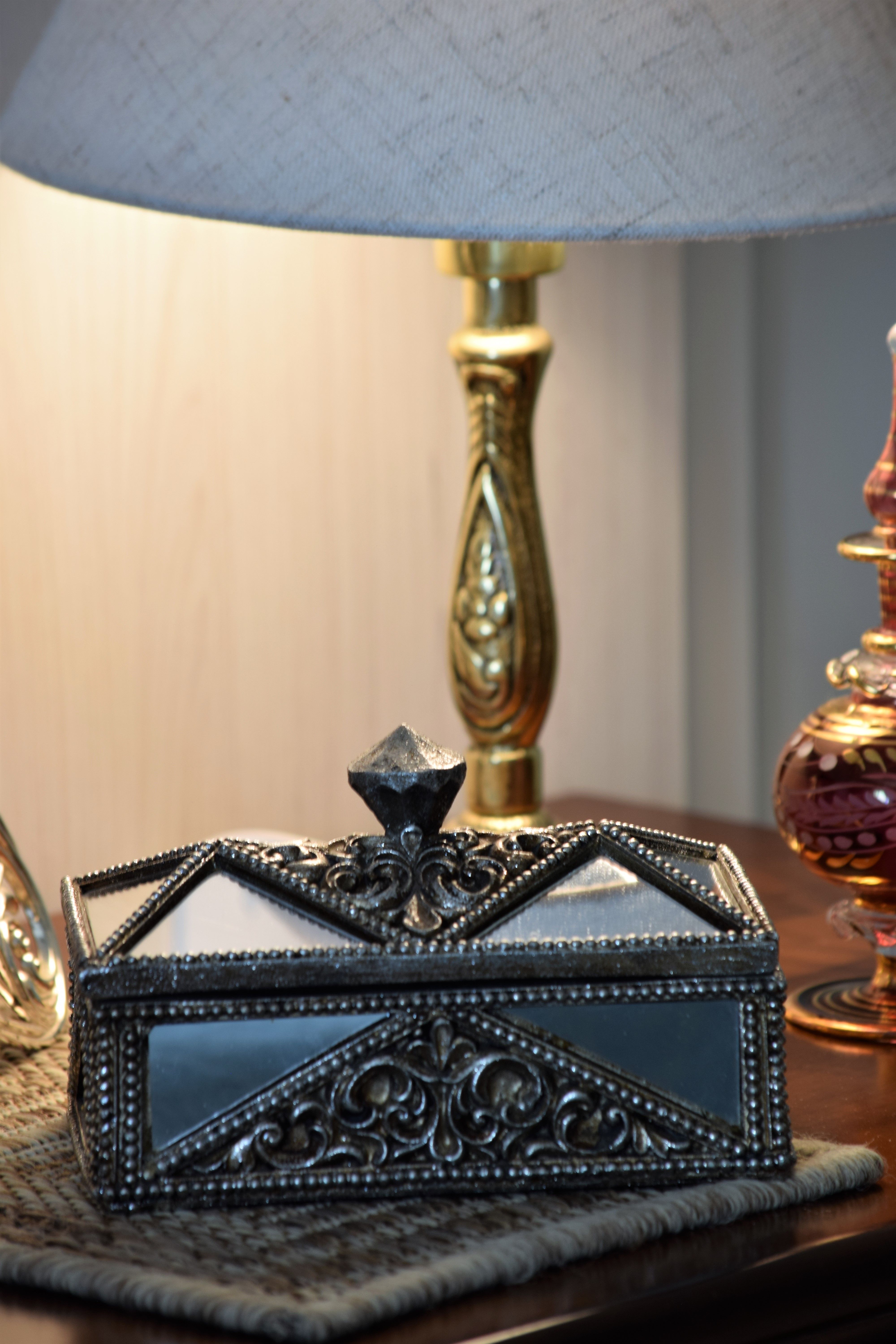 A detailed antique box, a family heirloom, on a table with a lamp, central to a son's proposal. A detailed antique box, a family heirloom, on a table with a lamp, central to a son's proposal.