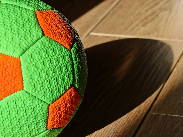 A green and orange ball on a wooden floor, casting a shadow, representing scary true stories.