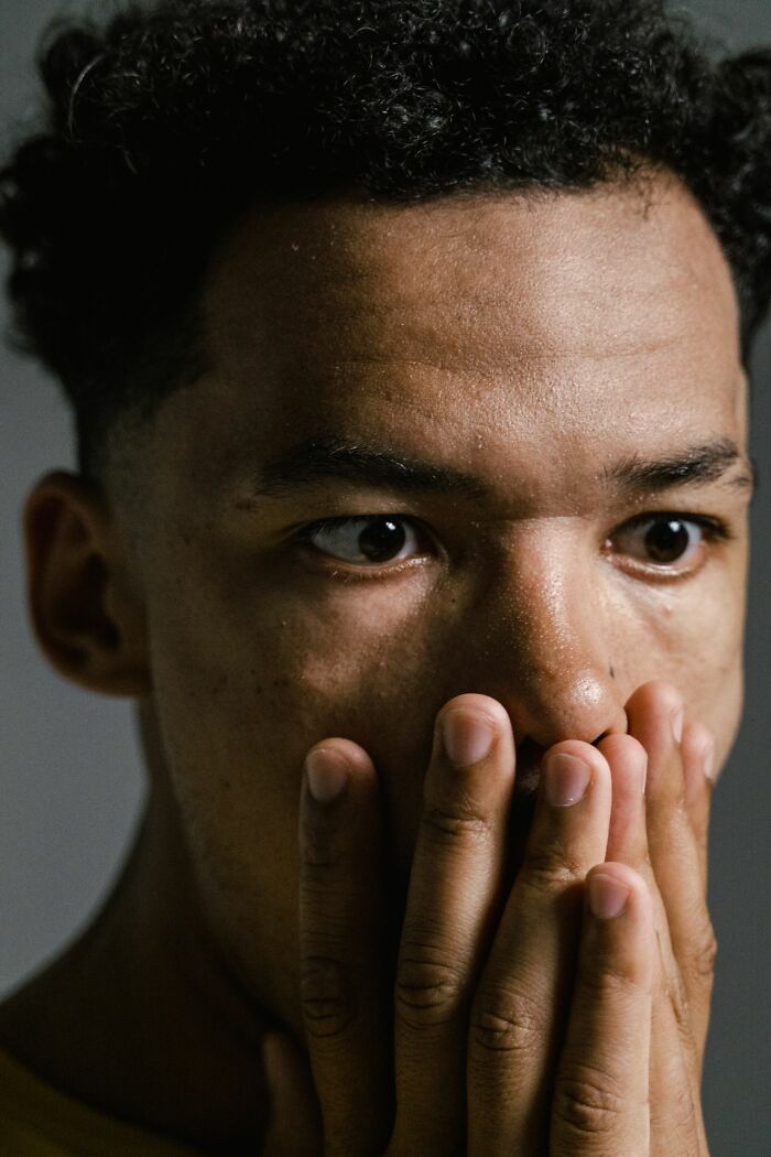 A man covers his mouth with his hands, wide-eyed, reflecting creepy true stories and questioning reality.