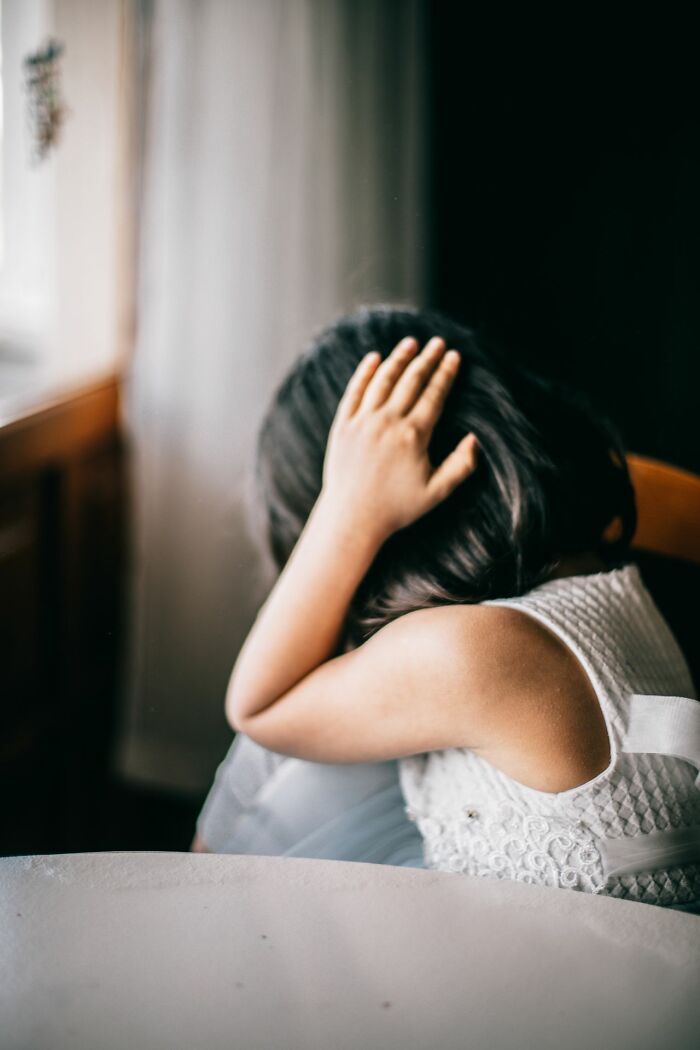 A young girl with dark hair covering her head with her hands, looking scared by a true story.