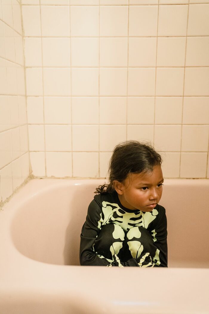 Young girl in a skeleton costume sitting in an empty bathtub, appearing scared from a creepy true story.