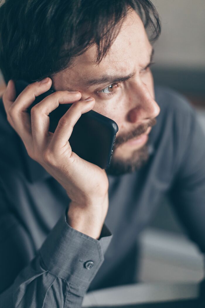 A man with a beard looks troubled while on a phone call, realizing he's with the wrong person.