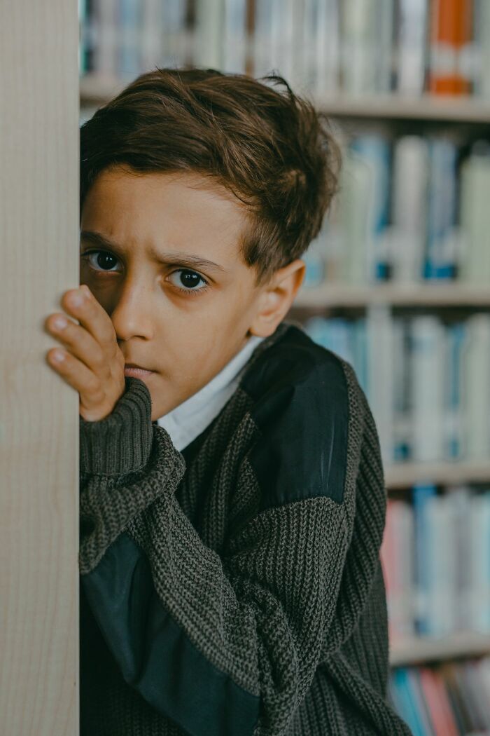 A boy peeks from behind a bookshelf with a scared expression, hinting at creepy true stories and questioning reality.