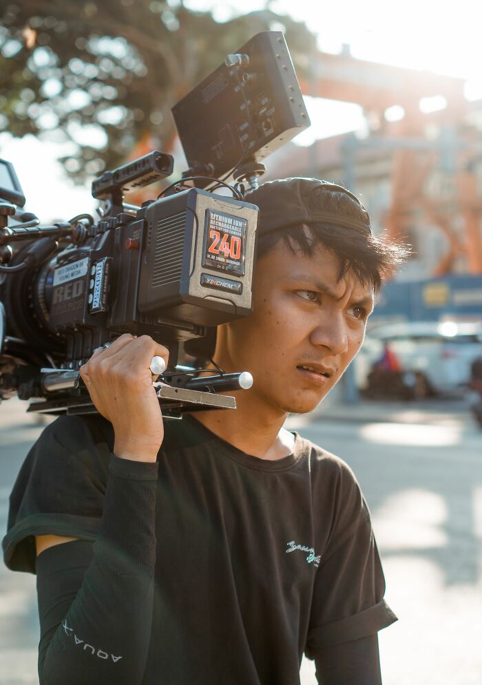 Man with a serious expression carrying a professional video camera on his shoulder, reflecting incredible accomplishments in filmmaking.