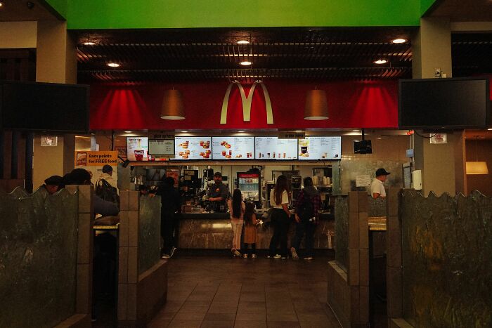 Interior of a McDonald's restaurant with a long counter and customers. Shows a popular fast-food drive-through location.
