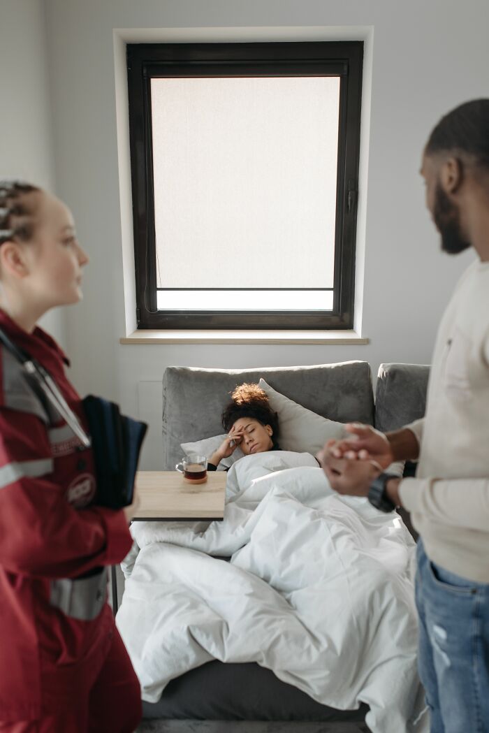 A woman, lying in bed looking unwell, attended by a man and an EMT, highlighting the exact moment a boyfriend said something.