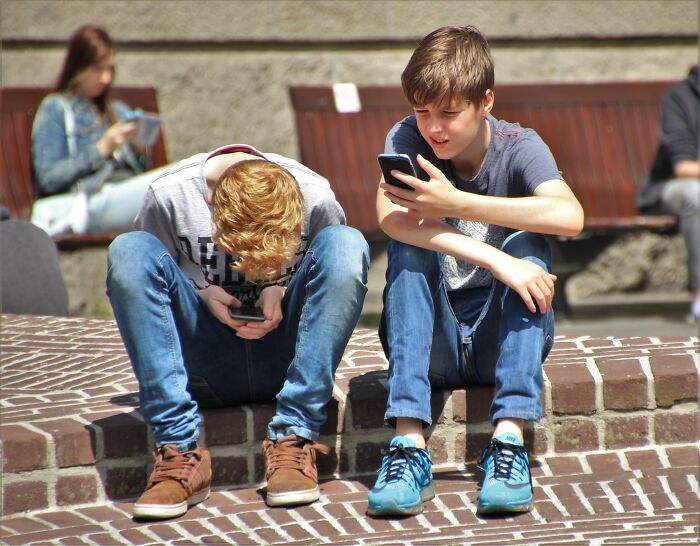 Two young boys looking at their phones outdoors, illustrating misconceptions about youth and technology.