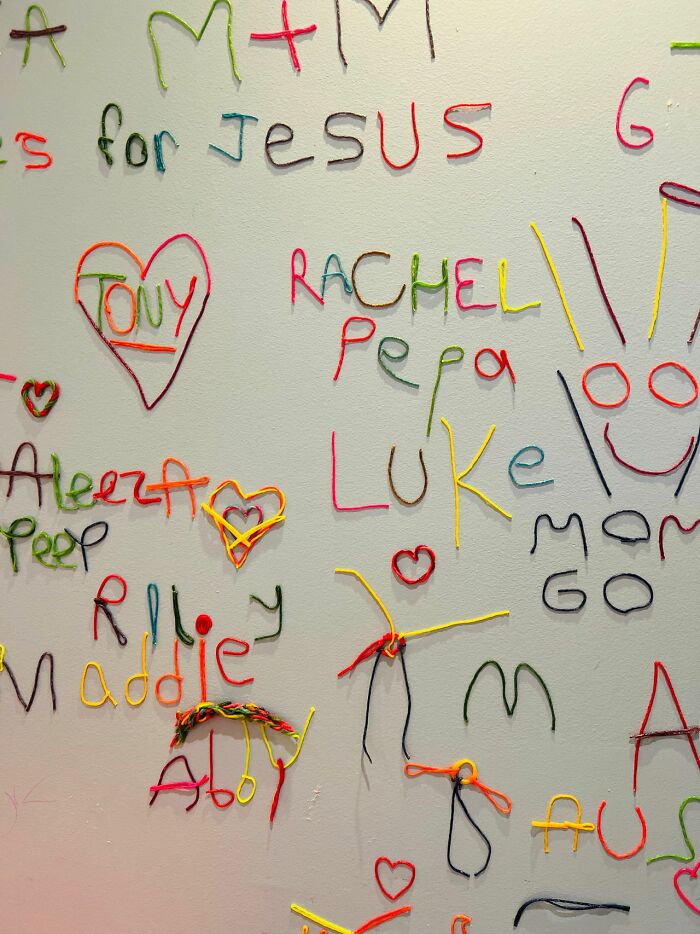 A wall covered in colorful yarn spellings of names and words, suggesting a horrible parent's chaotic home.