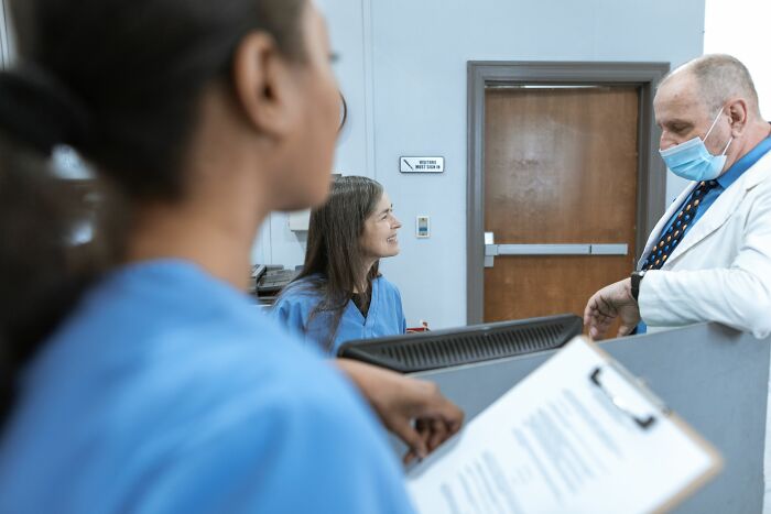 Medical staff conversing at a reception desk, avoiding sharing spicy personal details to prevent coworkers entering PTSD mode.