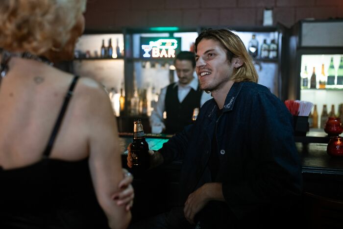 Man at a bar shares spicy personal details with a coworker, enjoying a drink.