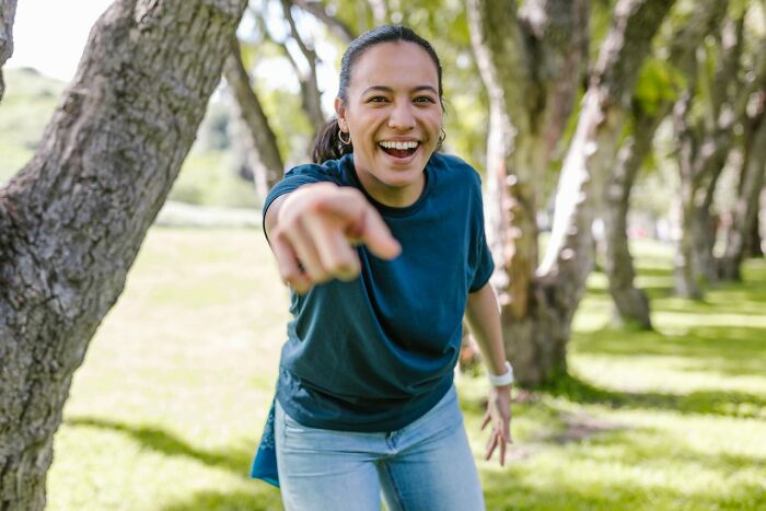 A woman in a park points forward with a wide smile. Horrible parent.
