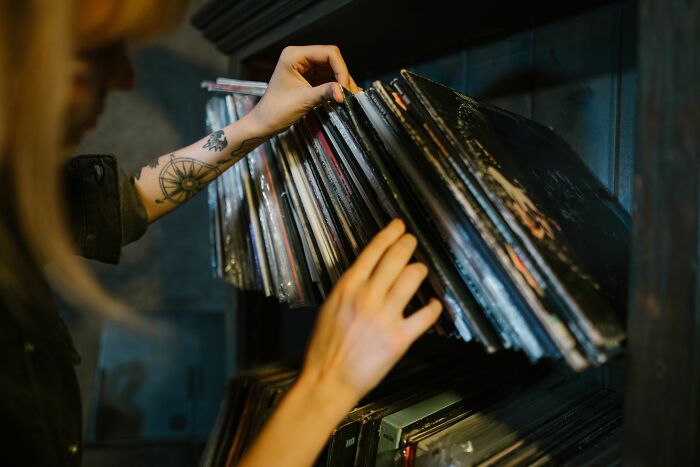 Person with a tattooed arm searching through a collection of '70s & '80s music records in a dimly lit room. Person with a tattooed arm searching through a collection of '70s & '80s music records in a dimly lit room.