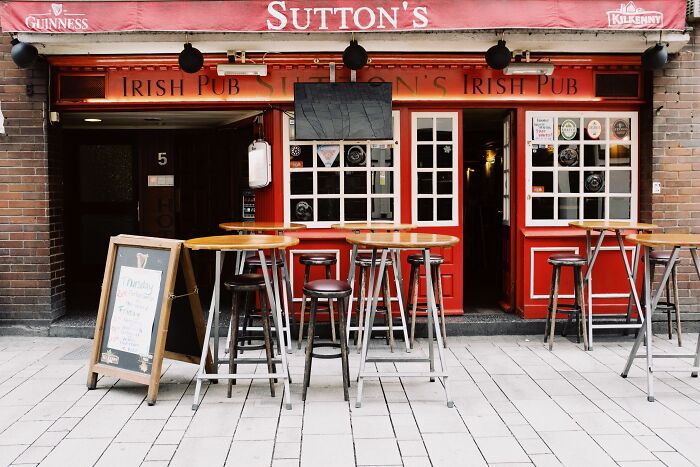 A red Irish pub with outdoor tables and stools, perfect for enjoying pub trivia questions and a drink.