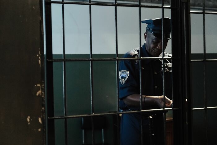 A prison guard in uniform stands behind metal bars, emphasizing the severity of a 100 years in prison sentence for a boy. A prison guard in uniform stands behind metal bars, emphasizing the severity of a 100 years in prison sentence for a boy.