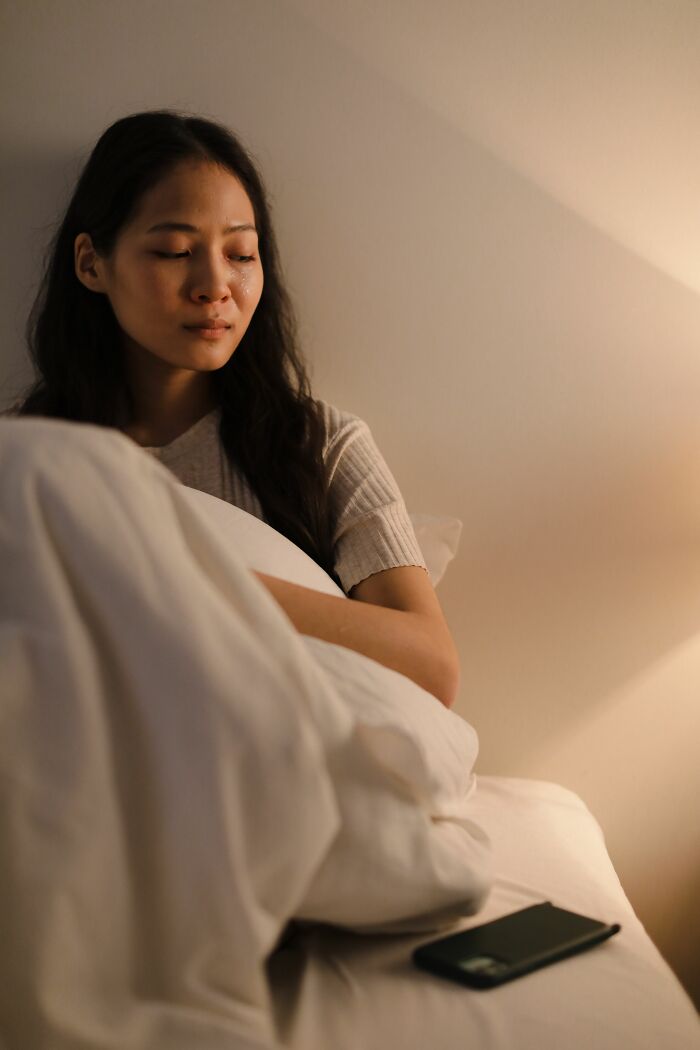 A woman sitting in bed looking upset, highlighting the emotional distress when a boyfriend says something unforgivable.