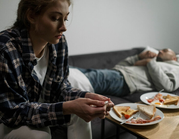 A woman sits on a couch, looking pensive, while a man lies in the background. She married her cousin. A woman sits on a couch, looking pensive, while a man lies in the background. She married her cousin.