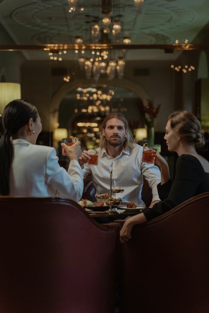 Three coworkers sharing spicy personal details while having drinks at a restaurant.