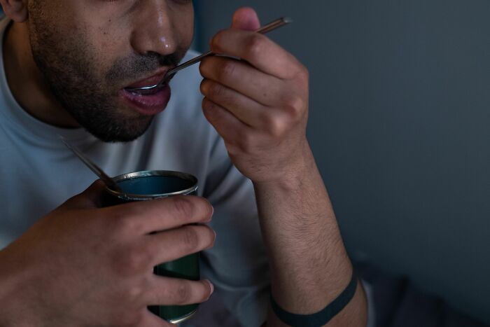 A man with a beard eating from a can with a spoon, symbolizing boring office moments and reading work drama stories.