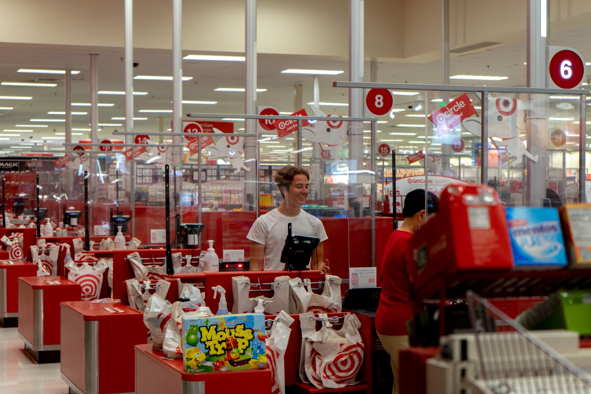 A shopper stands at a checkout counter in a busy store, bags on the counter.