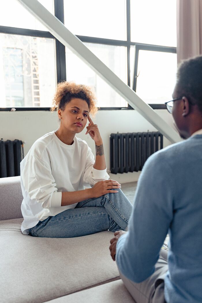 A woman sitting on a couch, talking to a man, realizing she is with the very wrong person.