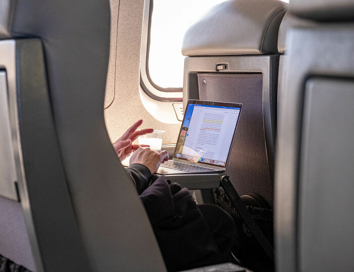 Person working on a laptop on an airplane during a flight, showing a typical airline environment.