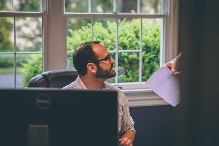 A man at a desk looking at a document, possibly related to work drama stories.