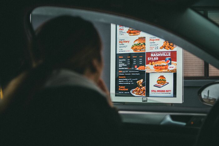 Customer in a car looking at a brightly lit drive-through menu, pondering crazy things customers said.