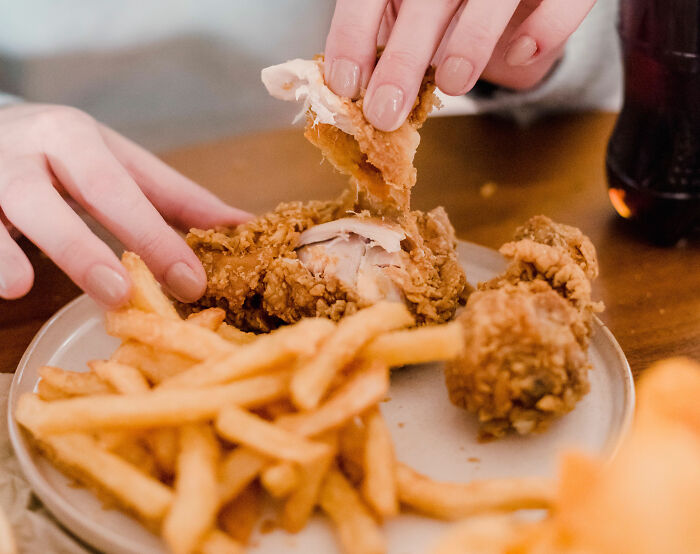 Hands breaking apart fried chicken with fries, representing a kid's school lunch often found in the USA. Hands breaking apart fried chicken with fries, representing a kid's school lunch often found in the USA.