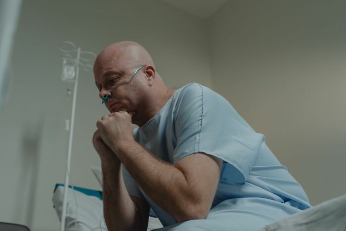 A patient, possibly a medical field worker, looks contemplative while wearing a nasal cannula in a hospital bed.