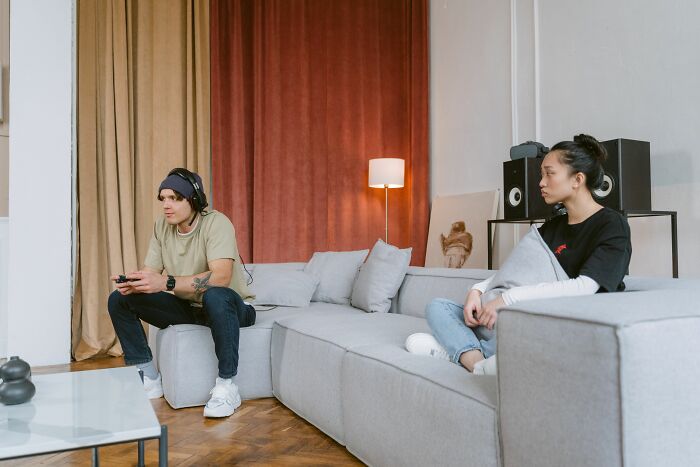 A couple on a couch, the man playing video games and the woman looking away, showing they’re with the very wrong person.