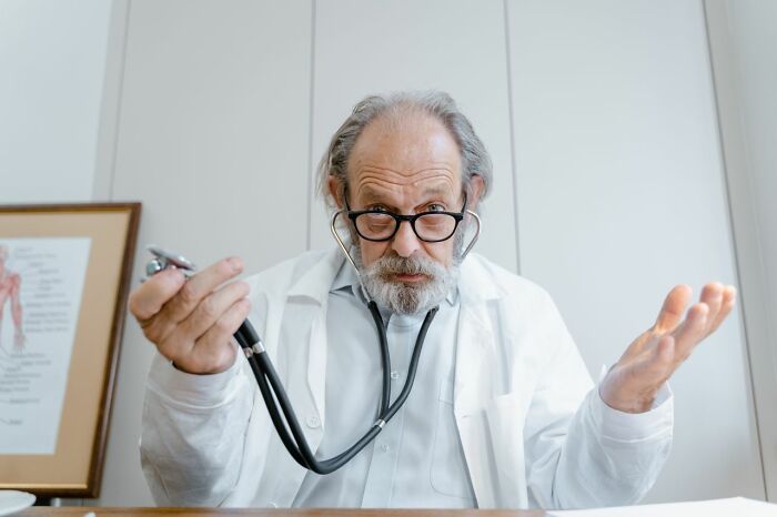 An older medical field worker shrugging with a stethoscope, conveying the challenges and frustrations medical workers encounter.