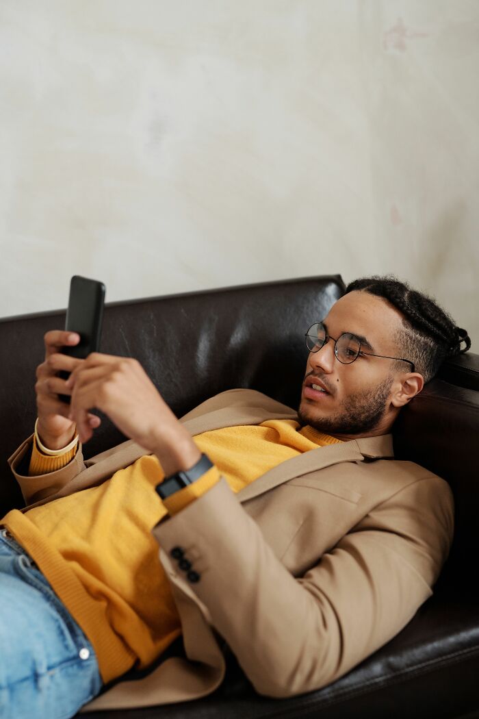 Man on a couch checking his phone, dealing with spicy personal details about coworkers.