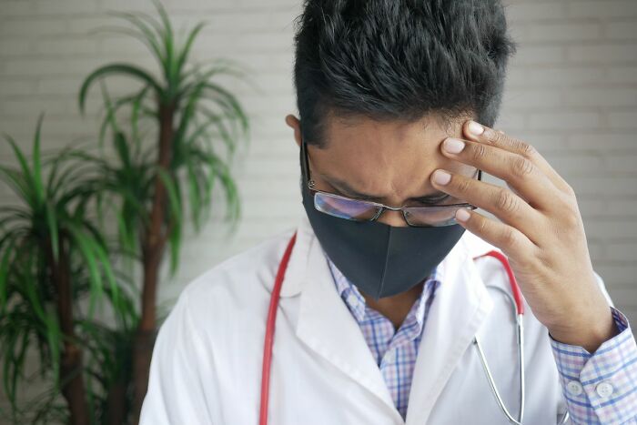 A medical field worker in a face mask looks stressed, holding his forehead. He represents the challenges medical field workers face.