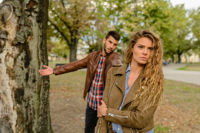 A man gesturing in frustration behind a woman with her arms crossed, depicting a difficult moment in a relationship.