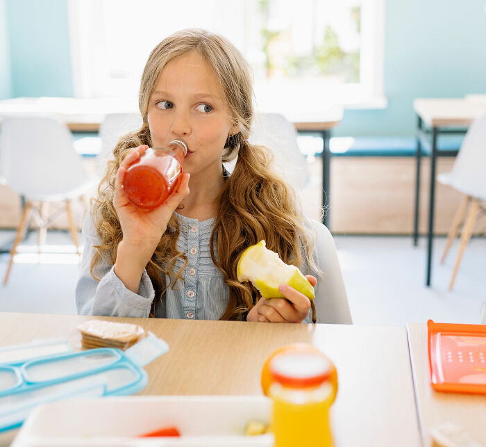 A child enjoying a school lunch with a drink and apple, contrasting French school lunch with USA options. A child enjoying a school lunch with a drink and apple, contrasting French school lunch with USA options.