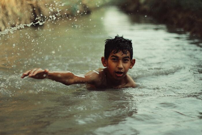 A young boy swimming in a shallow stream, representing stories of life and experiences.